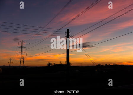 Tramonto colorato con elettricità tralicci e fili stagliano contro il cielo. Carr, County Down, N.Irlanda. Foto Stock