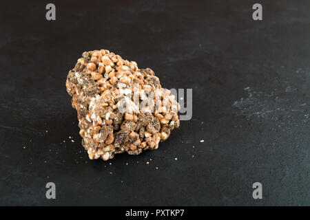 Un pezzo di cioccolato al latte con riso soffiato e uva passa su sfondo nero Foto Stock