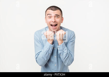 Uomo eccitato in maglietta blu in piedi con i pugni fino su sfondo bianco. Foto Stock