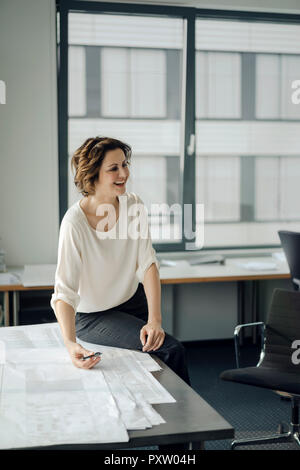 Imprenditrice seduta in ufficio, lavorando su blueprints Foto Stock