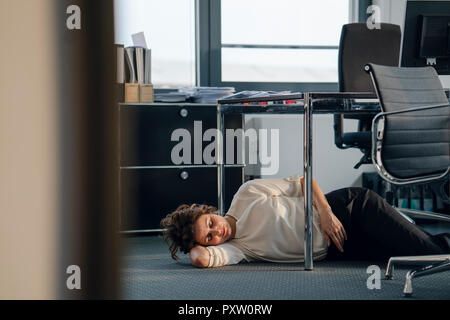 Stanco imprenditrice dormire sul pavimento sotto la scrivania Foto Stock