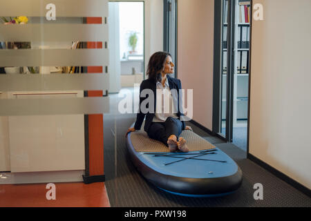 Imprenditrice seduta sulla scheda paddle, fantasticando in office Foto Stock