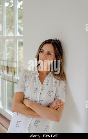 Malinconici donna matura a casa appoggiata contro una parete Foto Stock