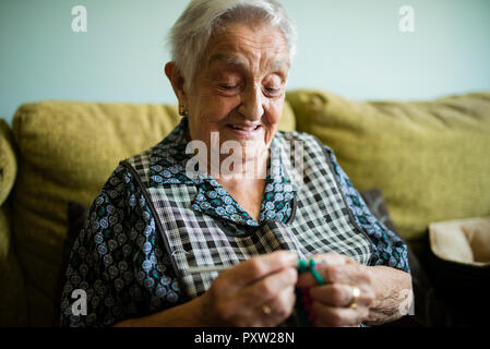 Ritratto di sorridente donna senior a crochet sul lettino a casa Foto Stock