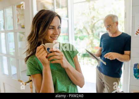 Coppia matura a casa con la donna a bere caffè e uomo quotidiano di lettura Foto Stock