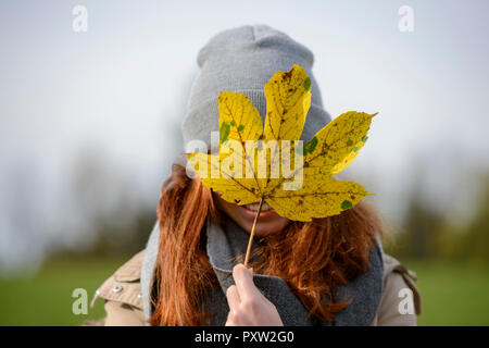 Ragazza adolescente nascondersi dietro a foglie di autunno Foto Stock