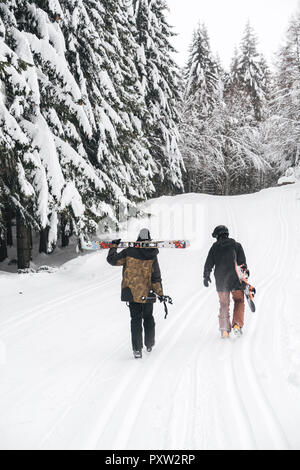 L'Italia, Modena, Cimone, vista posteriore del giovane con sci e snowboard e passeggiate nella foresta di inverno Foto Stock