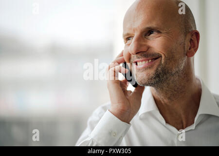 Imprenditore sorridente in piedi nel suo ufficio, parlando sul suo telefono cellulare Foto Stock