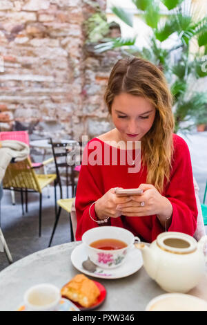 Giovane donna seduta al cafe' sul marciapiede utilizza lo smartphone Foto Stock