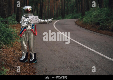 Spaceman autostop su Marte, in piedi sulla strada in foresta Foto Stock