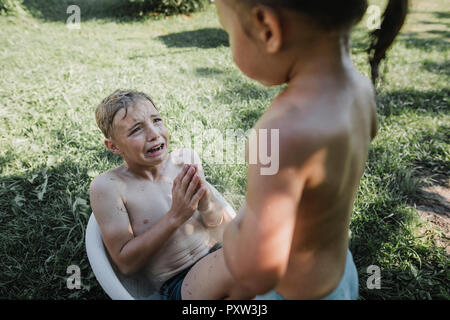 Fratello e Sorella gioca con acqua nella piccola vasca da bagno in giardino Foto Stock