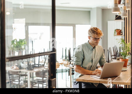 Giovane uomo che lavora nella sua start-up cafe, utilizzando laptop Foto Stock