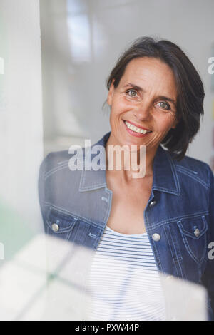 Ritratto di sorridere donna matura dietro il vetro di finestra Foto Stock