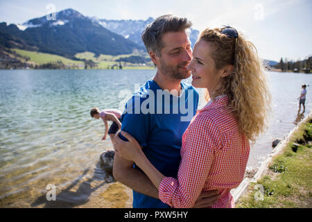 Austria, Tirolo, Walchsee, felice coppia abbracciando al lago con la famiglia in background Foto Stock