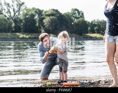 Padre e figlio divertendosi al Riverside, giocando con una pistola ad acqua Foto Stock