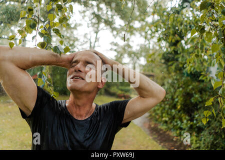 Sorridente uomo maturo godendo della pioggia di estate in giardino Foto Stock