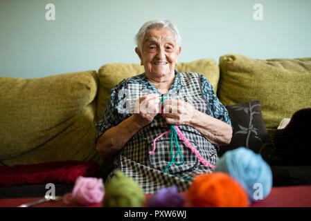 Ritratto di sorridente donna senior a crochet sul lettino a casa Foto Stock