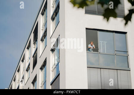 Uomo che parla al telefono, guardando fuori della finestra di ufficio Foto Stock