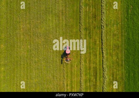 Top down vista aerea di un trattore rosso la coltivazione di terreni agricoli con una lama di filatura in Slovenia rurale Foto Stock