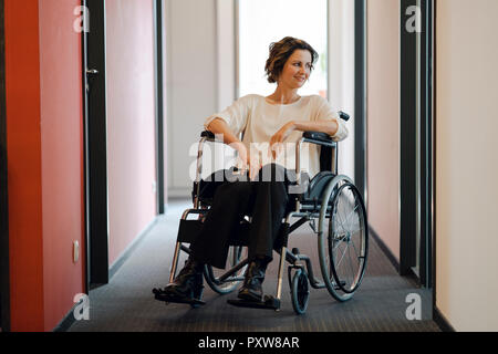 Disabili business donna seduta in sedia a rotelle e con il computer portatile sulle ginocchia Foto Stock