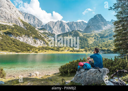 Austria, Tirolo, Escursionista prendendo una pausa, seduto su una roccia, guardando il lago Foto Stock