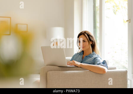 Donna matura seduti sul divano di casa utilizzando laptop Foto Stock