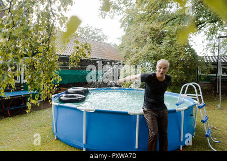 Ritratto di spensierata uomo maturo godendo della pioggia di estate in piscina in giardino Foto Stock