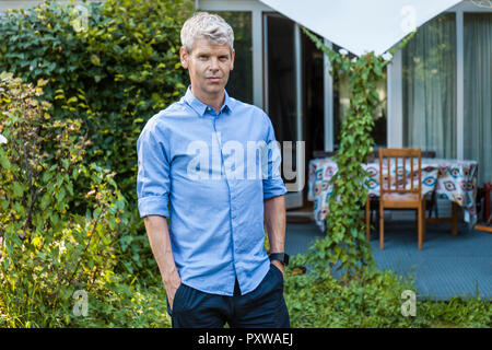 Ritratto di uomo maturo con i capelli grigi in piedi nel giardino della sua casa Foto Stock