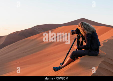 In Africa, la Namibia, il deserto del Namib Naukluft, Parco Nazionale, femmina photograper fotografare in Early Morning Light, seduti su una duna di sabbia Foto Stock