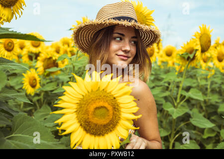 Giovane donna con un cappello di paglia sorridente in un campo di girasoli Foto Stock