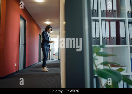 Imprenditrice matura in piedi nel corridoio di office, giocando con yoyo Foto Stock