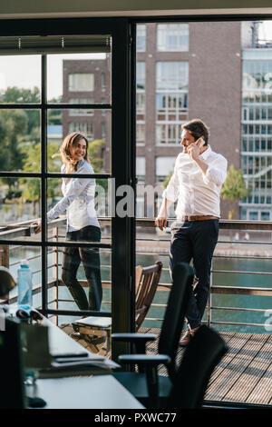 Imprenditore e la donna in piedi sul balcone, uomo di effettuare una chiamata Foto Stock