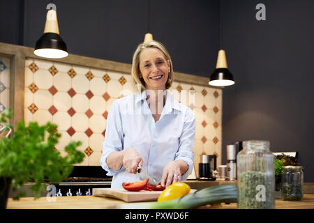 Ritratto di sorridere donna matura tritare il peperone in cucina Foto Stock