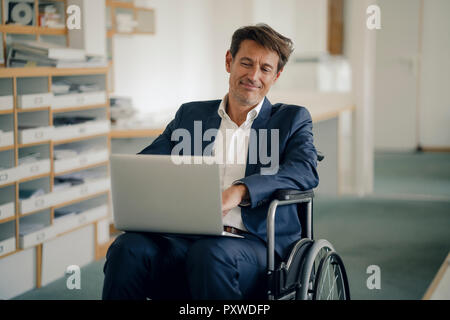 Imprenditore in carrozzella, utilizzando computer portatile in ufficio Foto Stock