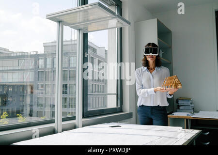 Donna che mantiene il modello architettonico della casa, utilizzando gli occhiali VR Foto Stock