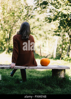 Vista posteriore della donna seduta sul banco di legno oltre ad una zucca Foto Stock