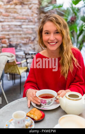 Ritratto di sorridente giovane donna con tazza da tè a pavement cafe Foto Stock