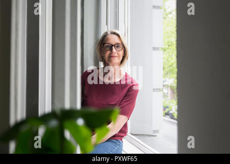 Ritratto di fiducioso donna matura in corrispondenza della finestra Foto Stock