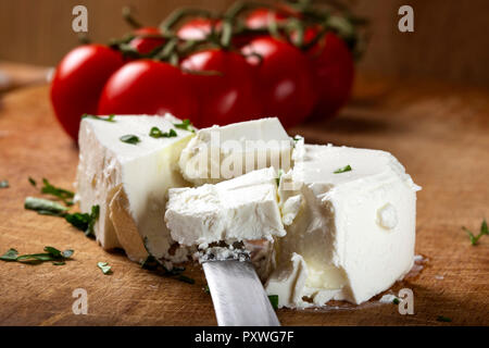 Pezzi di formaggio bianco su un tagliere di legno con pomodorini in background Foto Stock