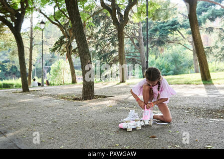 Bambina rosa legatura pattini a rotelle in un parco Foto Stock