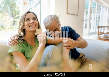 Giocoso uomo maturo di mordere nella donna di braccio di supporto carta di credito a casa Foto Stock