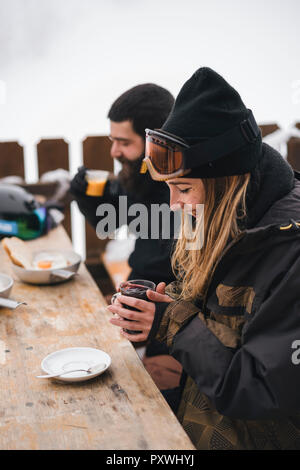 Matura in skiwear avente una bevanda calda al Mountain Lodge Foto Stock