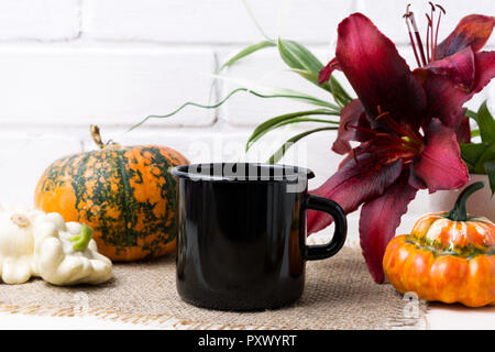 Nero smalto campfire tazza da caffè mockup con caduta di colore arancione zucca e giglio rosso. Boccale vuoto mock up per la promozione del design. Foto Stock