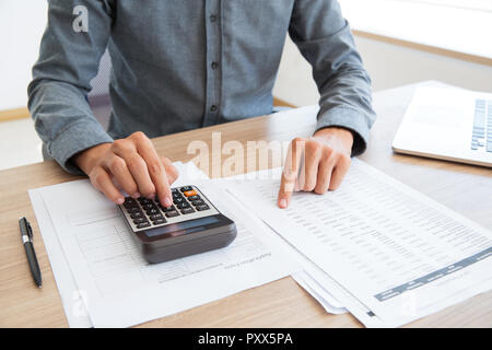 Close-up di un irriconoscibile uomo che lavora con i dati finanziari. Egli utilizzando una calcolatrice e esaminare il documento. Ispettore finanziario tenendo l'esame. La carta Foto Stock