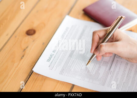 Mano con la penna sul viaggio Assicurazioni Aviazione modulo di domanda e il passaporto Foto Stock