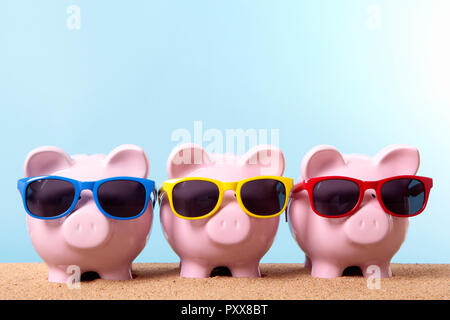 Tre rosa piggy banche su una spiaggia con occhiali da sole. Spazio per la copia. Foto Stock