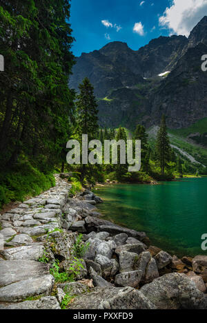 Percorso roccioso che conduce verso le alte montagne e con il lago accanto ad essa. Foto Stock