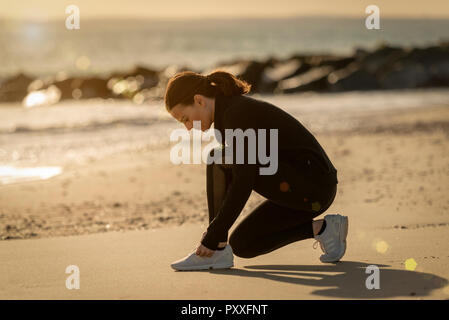 Pareggiatore donna regolare le sue scarpe prima di correre sulla spiaggia Foto Stock