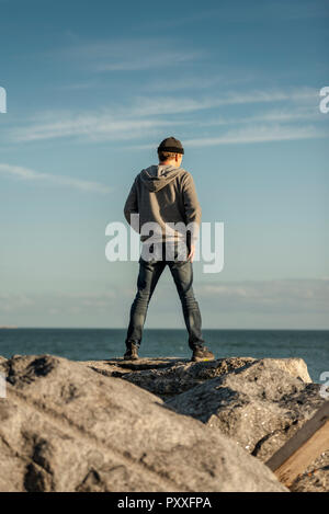 Vista posteriore di un uomo in piedi sulle rocce che guarda al mare Foto Stock