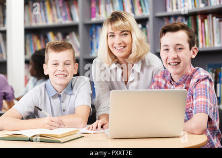 Ritratto di insegnante femminile aiutando due maschio di alta scuola gli studenti che lavorano al computer portatile in biblioteca Foto Stock
